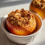 Close-up of a warm baked apple dessert topped with a golden, crunchy oat crumble filling.