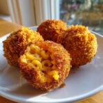 Four golden brown fried mac and cheese balls, one cut open to show melted cheese and macaroni inside.