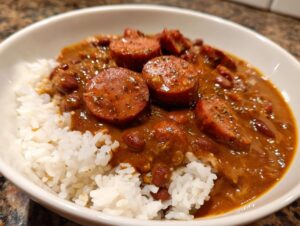 A close-up bowl of savory red beans and rice topped with thick slices of seasoned sausage.