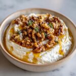 Close-up of a creamy ricotta dip topped with caramelized walnuts, honey drizzle, and fresh thyme sprigs.