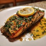 Close-up of a perfectly cooked salmon recipe fillet topped with garlic, parsley, and a lemon slice.