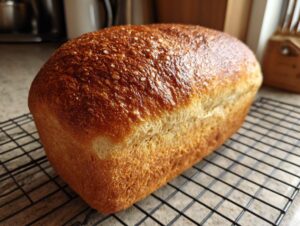 A freshly baked, golden-brown loaf of whole wheat bread resting on a black wire cooling rack.