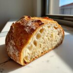 Close-up of a perfectly baked artisan bread loaf cut in half, showing an open, airy crumb structure.