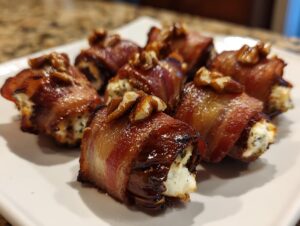 Close-up of several perfectly cooked bacon wrapped stuffed dates topped with walnuts on a white plate.