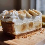A close-up slice of banana cream cheesecake showing layers of graham cracker crust, creamy filling, and fresh banana slices.