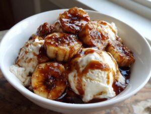 Close-up of warm, caramelized bananas foster slices served over scoops of melting vanilla ice cream in a white bowl.