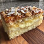 Close-up of a slice of bee sting cake showing layers of sponge, thick vanilla cream, and caramelized almond topping.