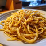 A close-up shot of a plate piled high with creamy caramelized onion pasta, seasoned with black pepper.