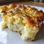 A close-up of a serving of baked mashed potatoes, topped with melted, browned cheese and sprinkled with dried herbs.