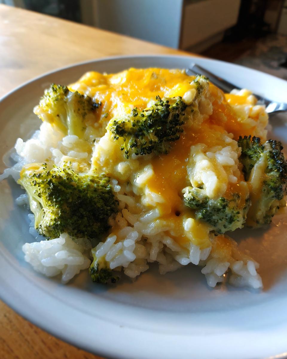 Close-up of a serving of cheesy broccoli rice on a white plate, featuring white rice, green broccoli florets, and melted cheddar cheese.