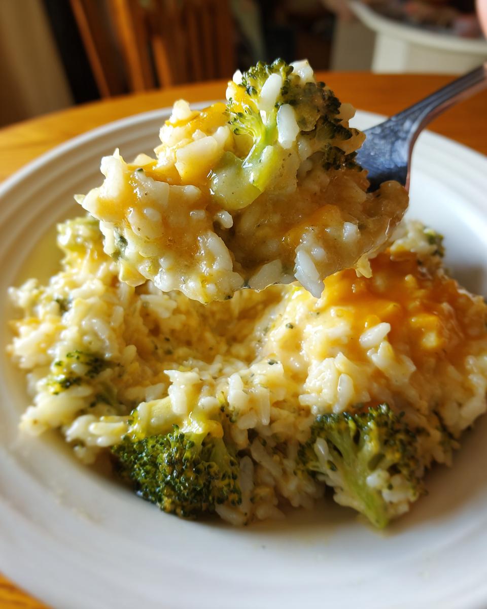 A fork lifting a creamy, cheesy scoop of broccoli rice from a white plate.