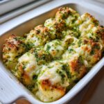 Close-up of baked hawaiian roll garlic bread covered in melted cheese and green herbs in a white dish.
