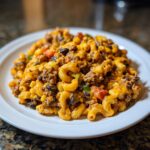 Close-up of a serving of cheesy taco pasta featuring elbow macaroni, ground beef, black beans, and corn on a white plate.