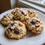 Close-up of several chewy almond joy cookies topped with chocolate chunks, sliced almonds, and coconut flakes.