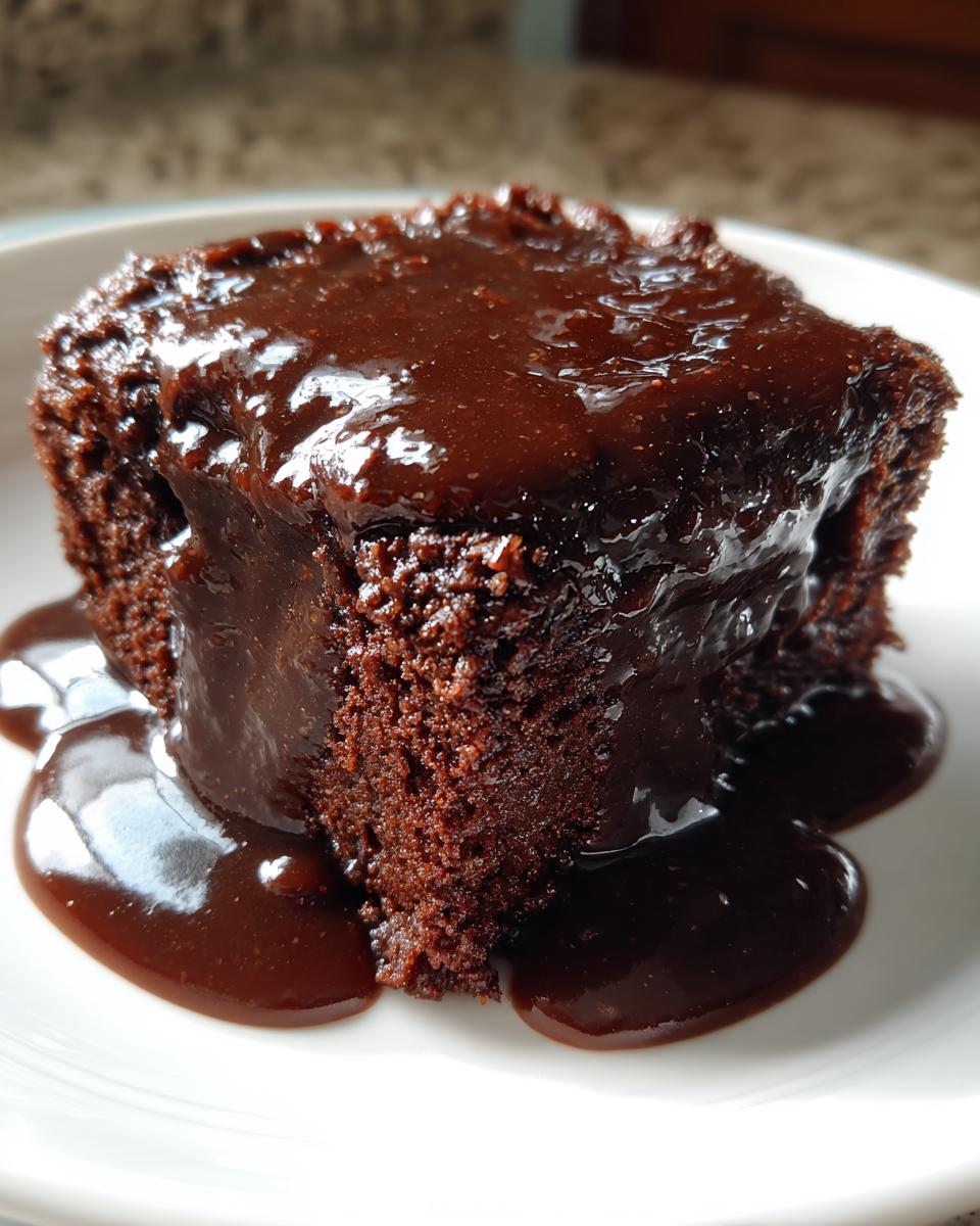 Close-up of a moist slice of chocolate pudding cake generously topped with glossy, dark chocolate sauce.