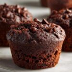 A close-up of a moist, dark chocolate zucchini muffin topped with melted chocolate chips.