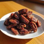 A pile of glistening, caramelized cinnamon sugar pecans coated in sparkling sugar crystals on a white plate.