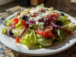 A close-up of a fresh copycat Olive Garden salad featuring crisp lettuce, red onion, tomatoes, olives, and shredded Parmesan cheese.