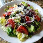 A close-up of a fresh copycat Olive Garden salad featuring crisp lettuce, tomatoes, red onion, olives, and grated Parmesan.