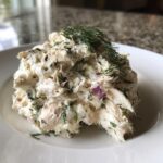 A mound of creamy cottage cheese chicken salad mixed with herbs and red onion, topped with fresh dill.
