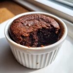 A rich, dark chocolate Cottage Cheese Microwave Brownie served warm in a white fluted ramekin with a bite taken out.