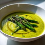 A vibrant green bowl of creamy asparagus soup topped with roasted asparagus spears and a drizzle of olive oil.