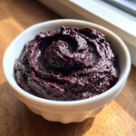 Close-up of a rich, dark purple, creamy black bean dip swirled in a small white bowl.