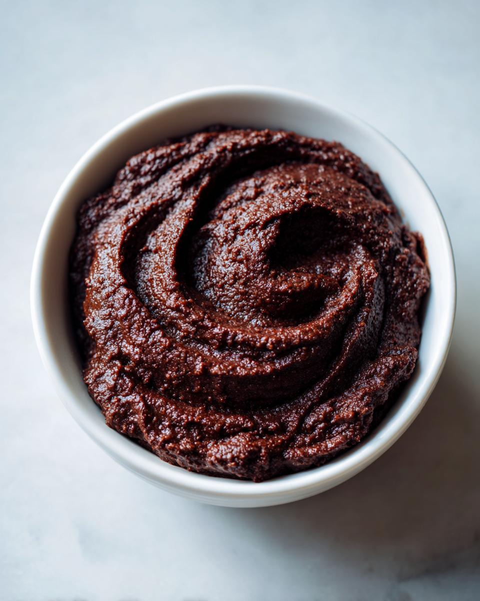 Overhead close-up of a white bowl filled with thick, dark brown, creamy black bean dip swirled on top.