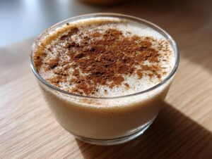 Close-up of a glass filled with creamy coquito recipe, topped generously with ground cinnamon.