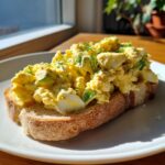 A generous serving of creamy egg salad piled high on a slice of toasted bread, garnished with fresh dill.