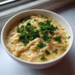 Close-up of a creamy bowl of lemon chicken soup featuring shredded chicken, orzo pasta, and fresh parsley garnish.