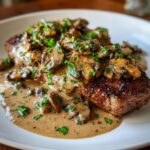 Close-up of a perfectly seared steak generously topped with creamy mushroom sauce and fresh parsley.