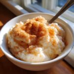 A close-up of creamy rice pudding recipe served in a white bowl, generously dusted with cinnamon.