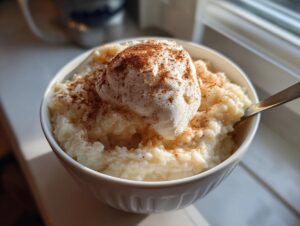 A close-up of a bowl of creamy rice pudding recipe, topped with whipped cream and sprinkled with cinnamon.