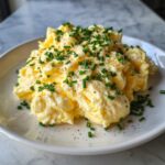 A close-up of fluffy, creamy scrambled eggs topped generously with fresh chopped chives and black pepper.