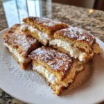 Four pieces of golden brown stuffed french toast filled with white cream cheese, dusted with powdered sugar.
