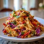 A vibrant mound of thai chicken salad featuring shredded chicken, red cabbage, peppers, and a peanut dressing, topped with crushed peanuts.