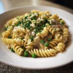 A close-up of creamy tuna pasta made with fusilli, green peas, and topped with fresh parsley.