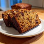 Two thick slices of moist date nut bread, packed with raisins and nuts, served on a white plate.