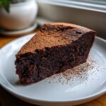 A rich, dark slice of flourless chocolate torte dusted generously with cocoa powder on a white plate.