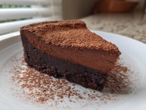 A rich, two-layered slice of flourless chocolate torte dusted heavily with cocoa powder on a white plate.