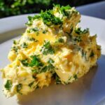 A mound of fluffy, yellow homemade garlic butter mixed with bright green chopped parsley, served on a white plate.