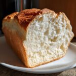Close-up of a freshly baked japanese milk bread loaf cut open, showing its incredibly soft, white, and fluffy interior crumb.
