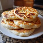 A stack of four golden-brown, puffy homemade pita bread rounds resting on a white plate.