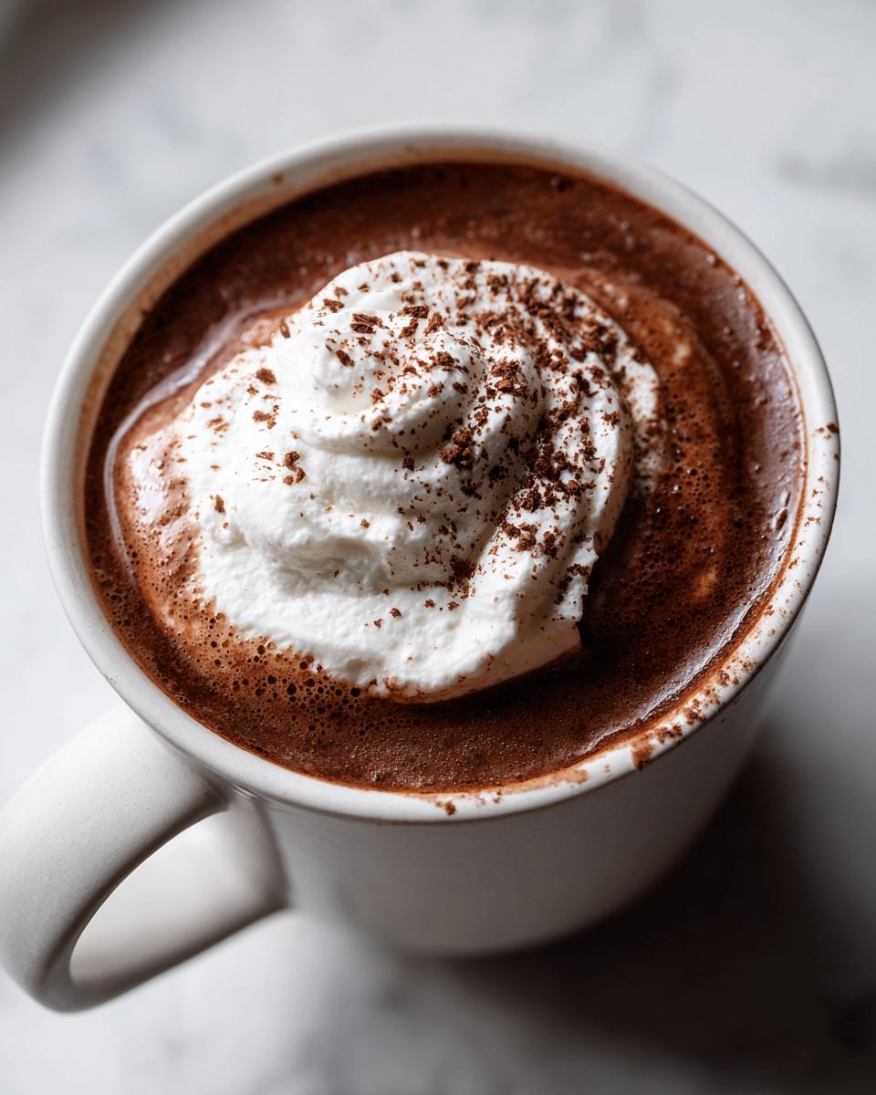 Overhead view of a mug filled with rich french hot chocolate topped with whipped cream and chocolate shavings.