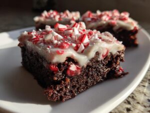 Close-up of a fudgy peppermint brownie slice topped with white frosting and crushed candy canes.