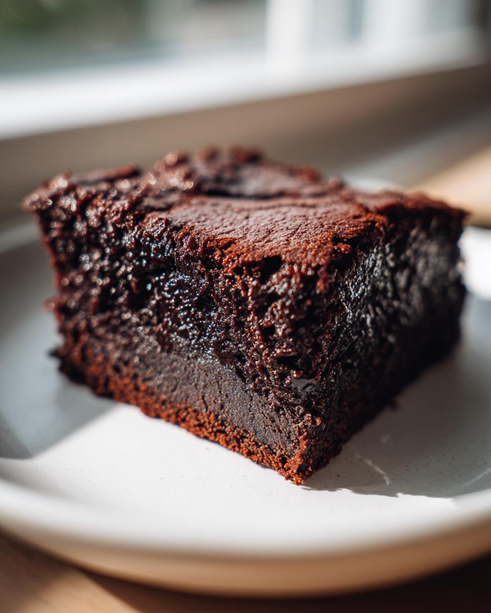 A close-up, richly textured slice of fudgy sweet potato brownies sitting on a white plate.