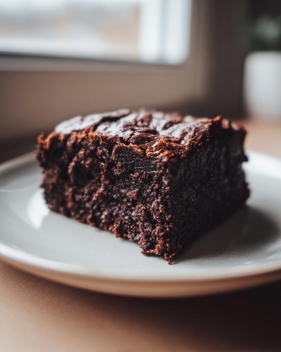 Close-up of a rich, dark, fudgy sweet potato brownies square on a light plate.