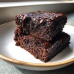 Two stacked, rich, fudgy sweet potato brownies with a glossy top, sitting on a white plate.