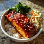 Close-up of a delicious salmon bowl featuring a piece of glazed salmon topped with sesame seeds over rice.